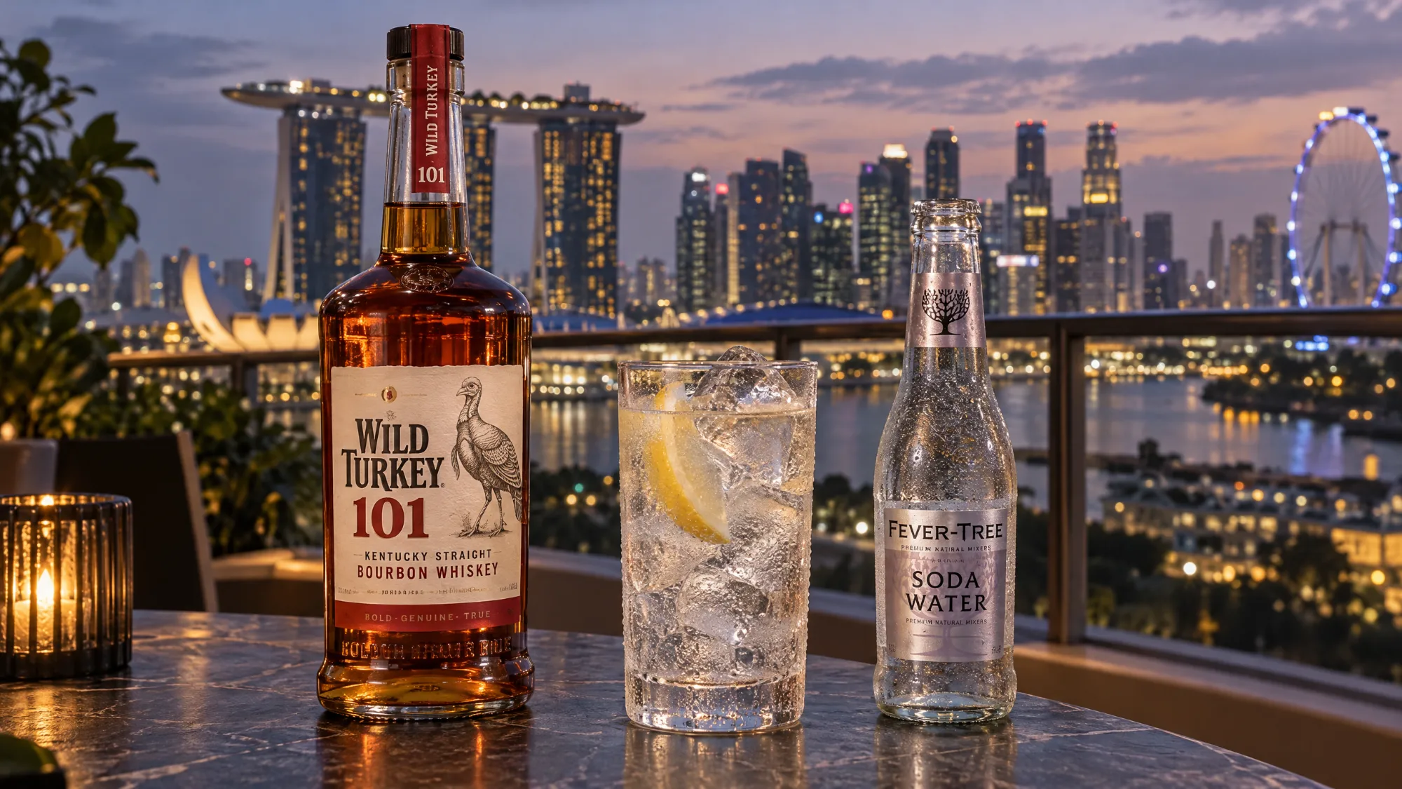A bottle of Wild Turkey 101 bourbon beside a tall highball with a lemon wedge and a bottle of Fever-Tree Soda Water, on a rooftop table with the Marina Bay skyline at dusk.