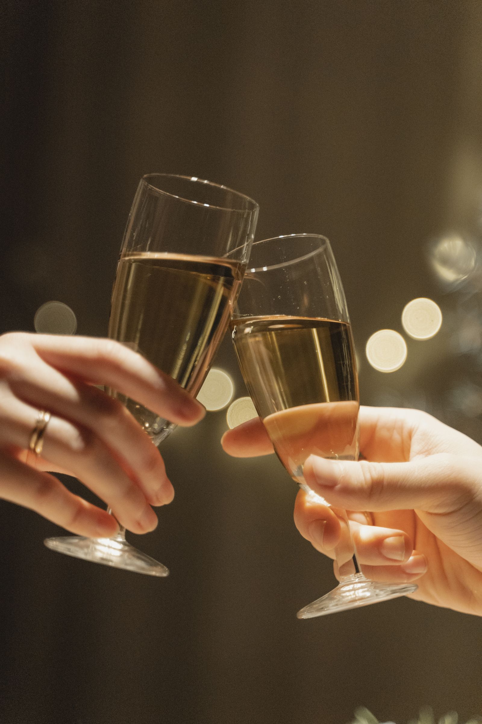 Close-up of hands clinking two champagne glasses together in a toast, warm bokeh background.